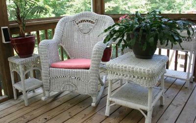 Un fauteuil en rotin blanc, tables latérales et plantes sur un porche en bois