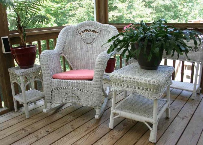 Un fauteuil en rotin blanc, tables latérales et plantes sur un porche en bois