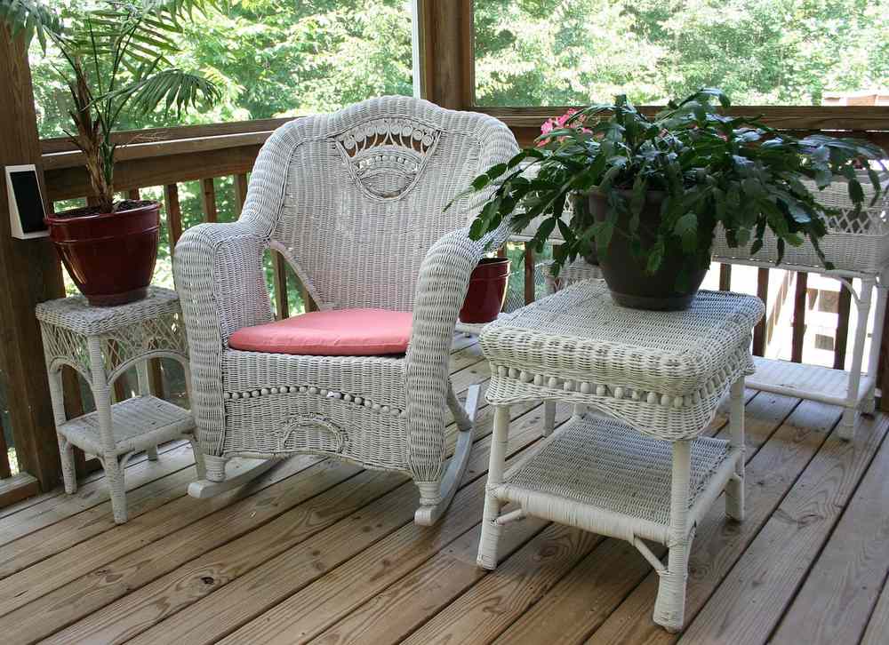Un fauteuil en rotin blanc, tables latérales et plantes sur un porche en bois